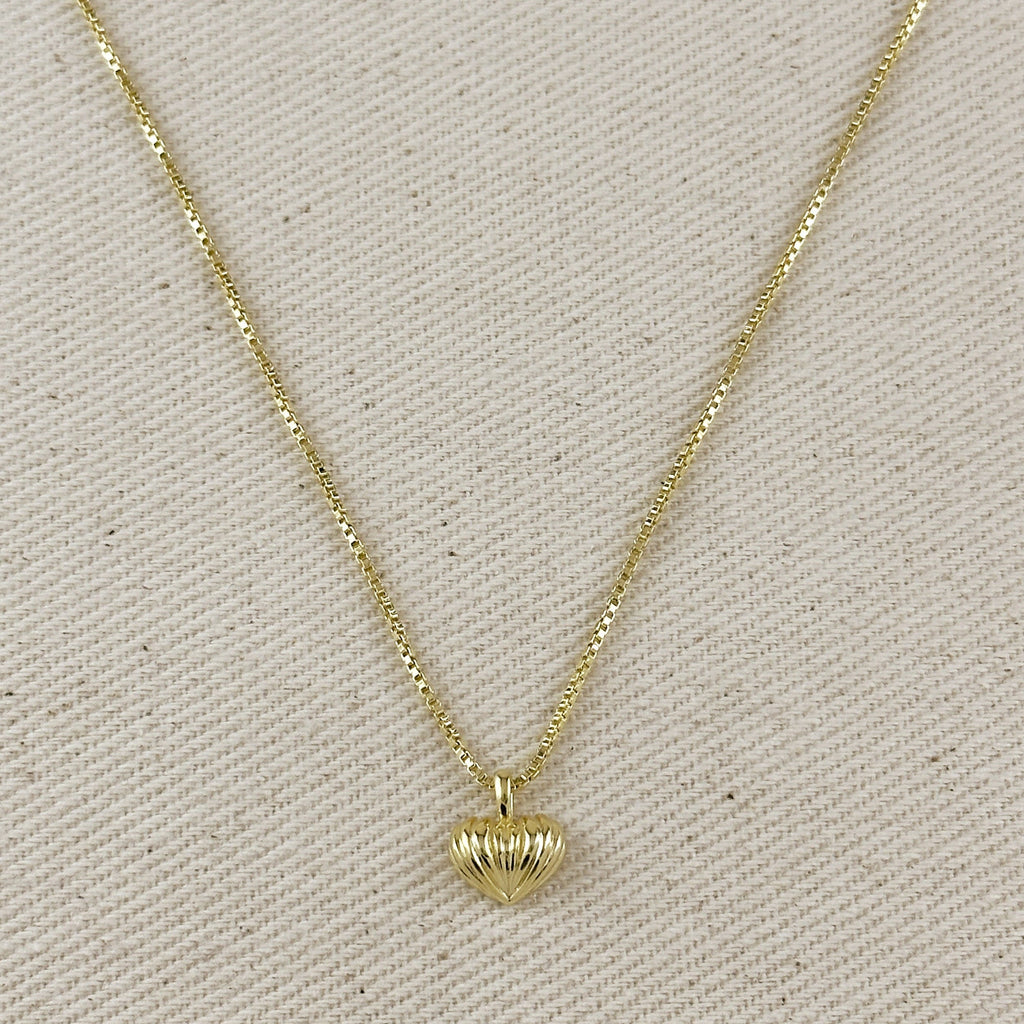 Gold necklace with a heart-shaped pendant on a beige fabric background