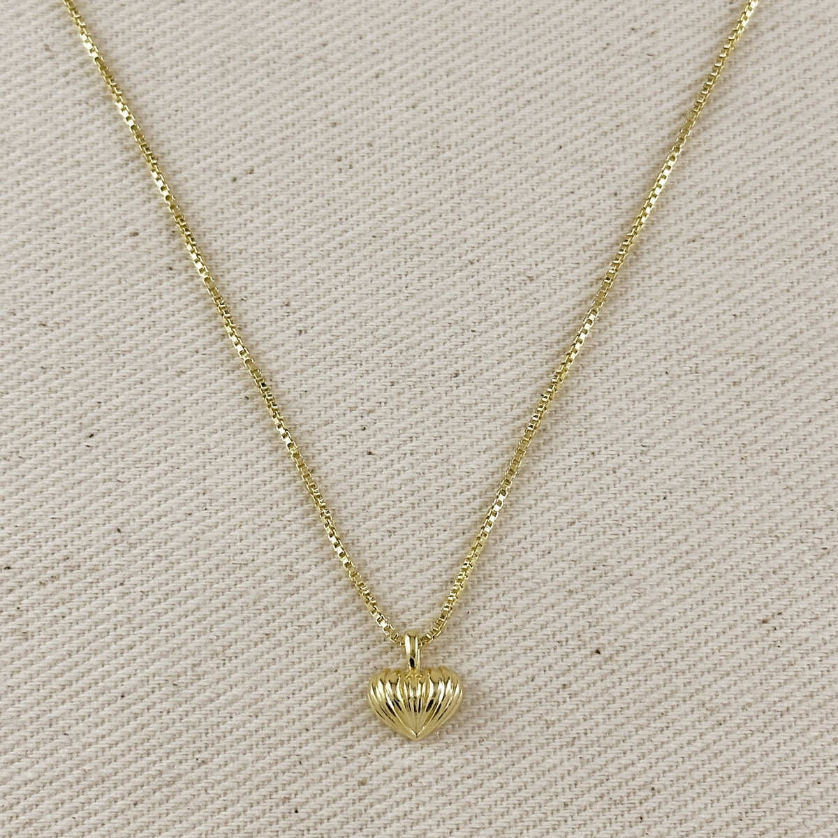 Gold necklace with a heart-shaped pendant on a beige fabric background