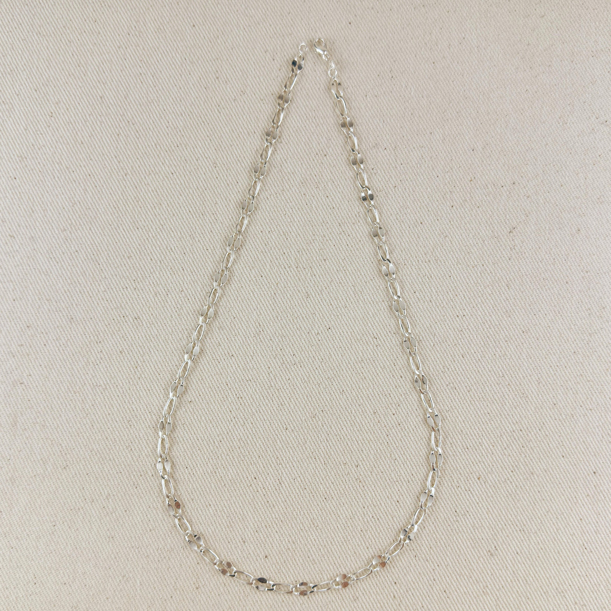 Silver chain necklace on a light beige fabric background