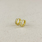 Gold hoop earrings with embedded stones on a beige fabric background
