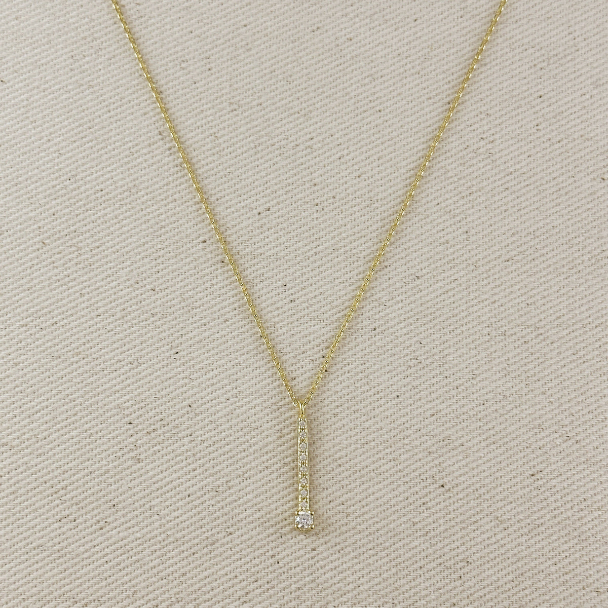 Gold necklace with a small diamond pendant on a beige fabric background
