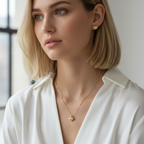 Woman wearing a gold necklace with a heart pendant in a softly lit room.