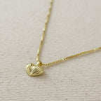 Gold necklace with a heart-shaped pendant on a light beige background