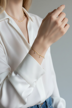 Person wearing a white shirt with a focus on jewelry, including a necklace and bracelet.