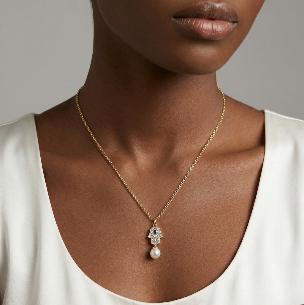 Woman wearing a gold necklace with a Hamsa pendant featuring pearls against a neutral background