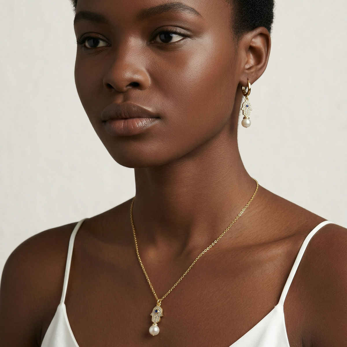 Woman wearing a gold necklace and earrings against a neutral background