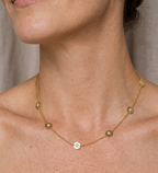 Gold necklace with a central pendant on a person's neck against a neutral background