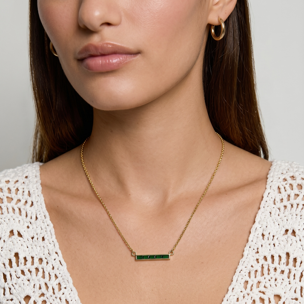 Woman wearing a gold necklace with a green gemstone on a plain background