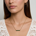 Woman wearing a gold necklace with a green gemstone on a plain background