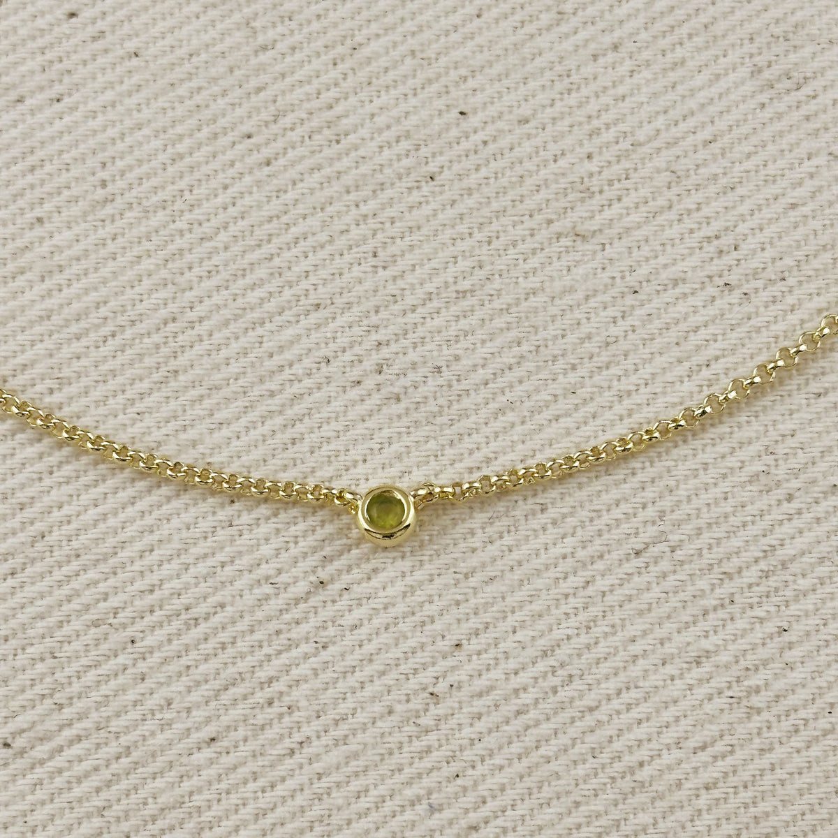 Close-up of 18K gold filled dainty necklace featuring a bezel setting, showcasing a cubic zirconia birthstone.