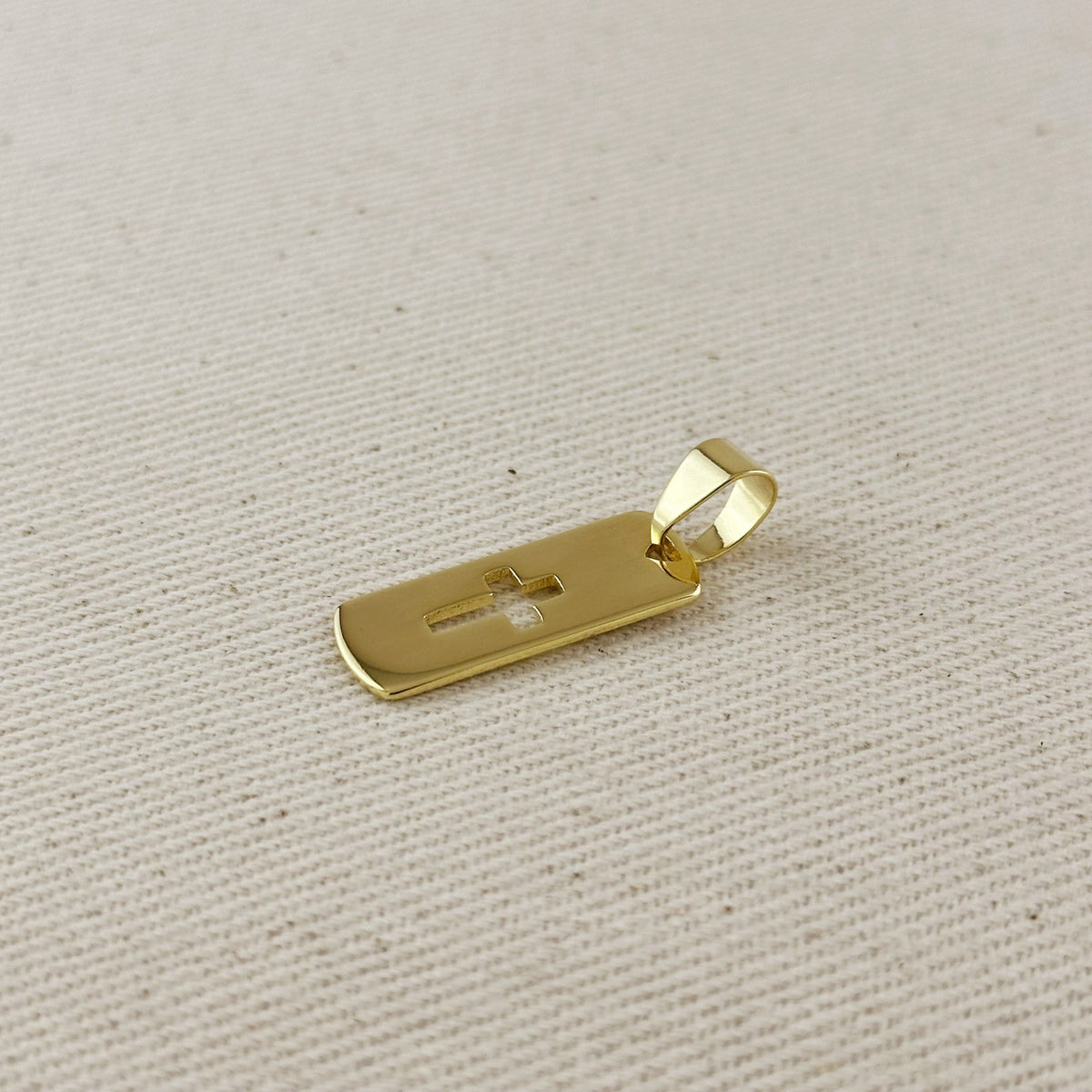 Gold pendant with a cross on a beige fabric background