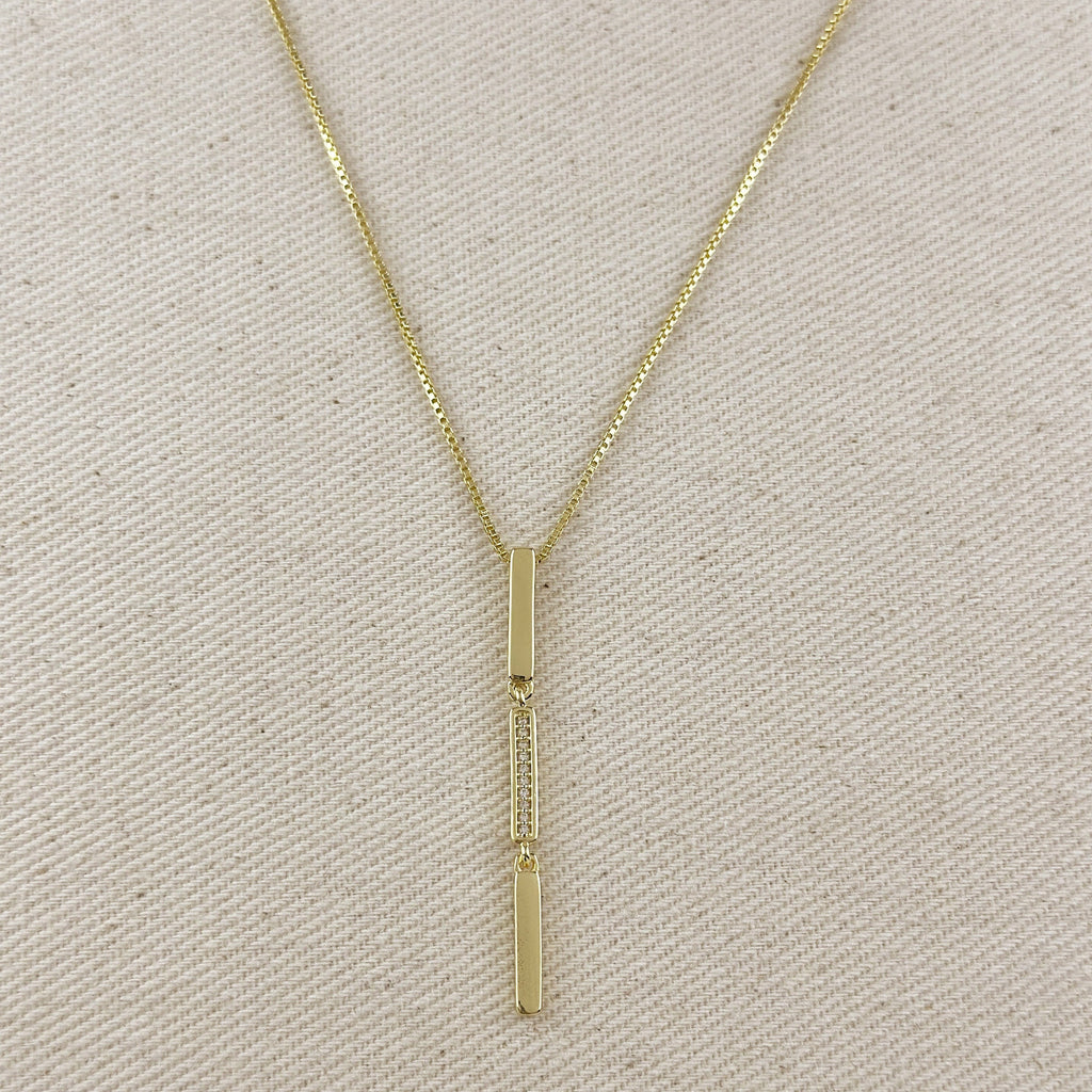 Gold necklace with a vertical pendant on a beige fabric background