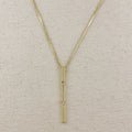 Gold necklace with a vertical pendant on a beige fabric background
