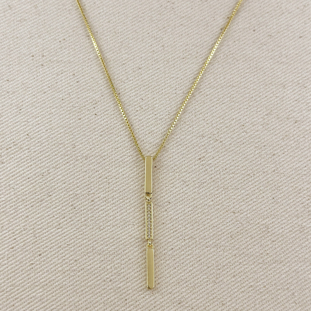Gold necklace with a vertical pendant on a beige fabric background