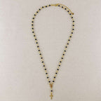 Necklace with black and gold beads and a cross pendant on a light gray background